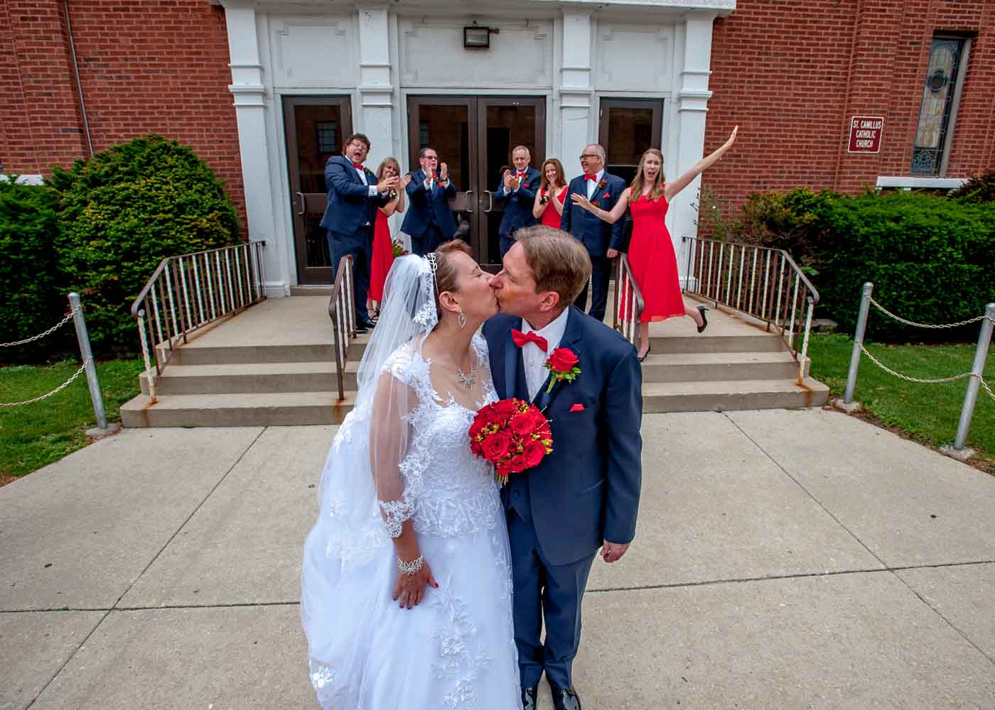 Bride and groom kissing with wedding party behind in front of church entrance